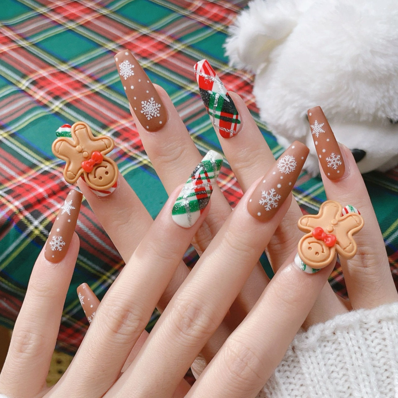 Festive Christmas nails featuring gingerbread man designs, with brown, white, and red accents, decorated with tiny candy-like details and holiday-themed patterns.