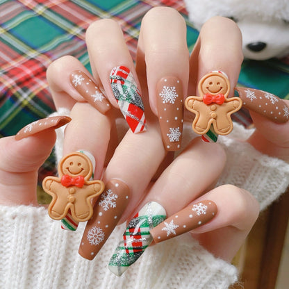 Festive Christmas nails featuring gingerbread man designs, with brown, white, and red accents, decorated with tiny candy-like details and holiday-themed patterns.