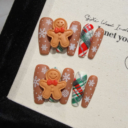 Festive Christmas nails featuring gingerbread man designs, with brown, white, and red accents, decorated with tiny candy-like details and holiday-themed patterns.